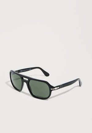 Lunettes de soleil rectangulaires noires avec des verres vert foncé et des détails décoratifs blancs sur les branches, présentées sur un fond blanc.