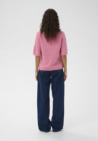 Rosa Kurzarm-Pullover aus weichem Strickmaterial, kombiniert mit locker sitzenden dunkelblauen Jeans aus Denim. Einfaches und legeres Design.