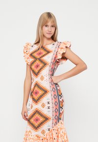 Χρωματιστό φόρεμα με μείγμα γεωμετρικών μοτίβων σε πορτοκαλί και ροζ τόνους, με φουσκωτά μανίκια και φαρδύ τελείωμα. Κατασκευασμένο από ελαφρύ ύφασμα.