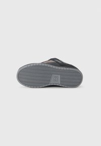 Zapatilla negra con una parte superior texturizada, que presenta una suela de goma gris y un patrón de banda de rodadura en zigzag. Incluye un acento de logo naranja.