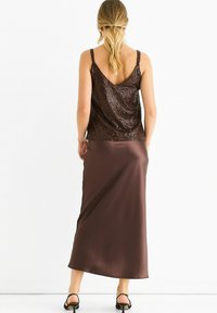 Brown sequined tank top with a v-neck and thin straps paired with a long, smooth, brown satin skirt. Worn with black sandals.
