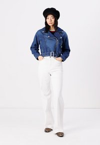 Denim dviračių striukė su diržu juosmenyje, mėlynos spalvos, su užtrauktuku priekyje ir ilgomis rankovėmis. Derinama su aukštuose liemenyje baltais platėjančiais kelnais ir leopardų rašto batais.