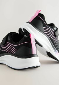 Baskets de sport noires avec des rayures roses, dotées d'une tige texturée et d'une semelle intermédiaire blanche. Comprend une languette rose au talon pour un enfilage facile.