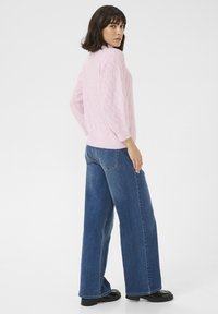 Maglione texturizzato rosa chiaro con un motivo a treccia, abbinato a jeans a gamba larga blu e scarpe con plateau nere.