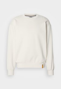 Λευκή μπλούζα με στρογγυλή λαιμόκοψη, ραμμένα μανίκια και τελείωμα, διαθέτει μία μικρή κίτρινη ετικέτα λογότυπου στην αριστερή πλευρά. Λεπτή υφή.