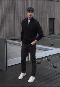 Schwarze Zip-Up Jacke, schlanke schwarze Hose und weiße Sneakers. Runder Hut. Glattes Material mit einer taillierten Silhouette. Minimalistisches Design ohne Muster.