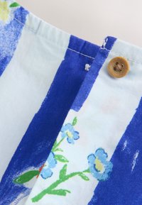 Detail modrobíle pruhované látky s malým modrým květinovým potiskem a béžovým knoflíkem na rohu.