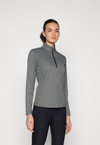 Fekete-fehér, cipzáros, hosszú ujjú felső, kockás mintával, magas gallérral és rugalmas anyaggal, fekete nadrággal párosítva.