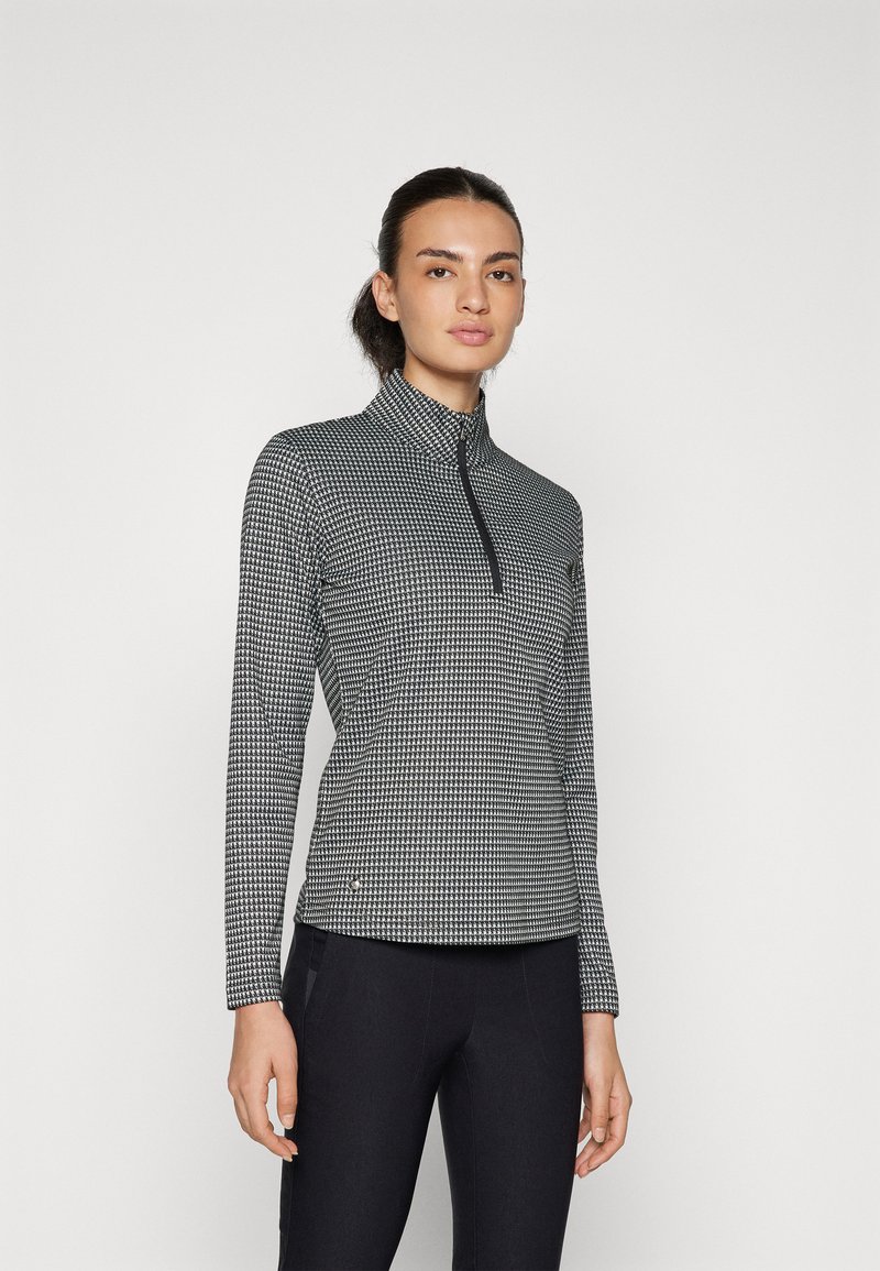 Fekete-fehér, cipzáros, hosszú ujjú felső, kockás mintával, magas gallérral és rugalmas anyaggal, fekete nadrággal párosítva.