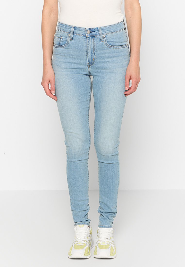 Jeans ajustados de color azul claro, confeccionados en denim, con diseño de cinco bolsillos, un sutil desvanecimiento y un corte ajustado. Combinados con zapatillas blancas y amarillas.
