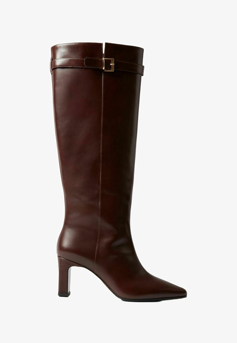 Bota de cuero marrón hasta la rodilla con punta afilada, que presenta un diseño elegante, un tacón corto apilado y un acento de cinturón cerca de la parte superior.