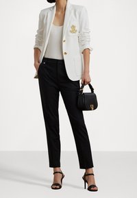 Vit blazer med broderad fickdetalj, kombinerad med en figurnära svart linne, skräddarsydda svarta byxor och en liten svart handväska.