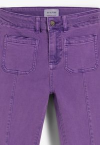 Vaqueros de mezclilla morados con cinco bolsillos, cierre de botón de metal y detalles de costura sutiles a lo largo de las costuras. Etiqueta de la marca visible en la cintura.