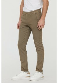 Beige, slim-fit chinos med knappstängning, sidofickor och uppvikta fållar, kombinerat med vita sneakers med bruna detaljer.