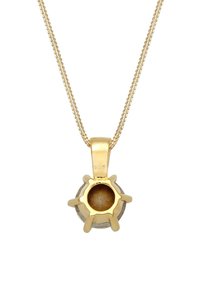 Collier pendentif doré avec une forme ronde, présentant une surface texturée et un motif en éclat de soleil. Attaché à une chaîne délicate.