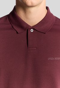 Bordeaux polo skjorte lavet af glat stof, med en klassisk krave, en knaplukning og LYLE & SCOTT-logoet i en kontrastfarve.