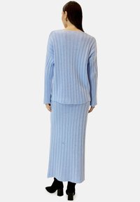 Ensemble pull en maille côtelée bleu clair et jupe assortie, avec manches longues, coupe décontractée et texture douce. Porté avec des talons blocs noirs.