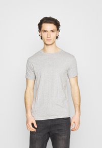 Camiseta de algodón gris con mangas cortas y cuello redondo, que presenta una textura suave y una forma ajustada, combinada con jeans oscuros.