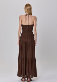 Robe maxi marron à volants, sans bretelles, avec un buste froncé et des liens réglables au cou. Tissu fluide avec une texture douce.