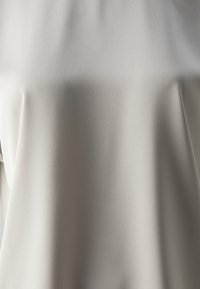 Svijetlosiva bluzica od glatkog, teksturiranog materijala; dizajnirana s opuštenim krojem i bez istaknutih detalja ili ukrasa.