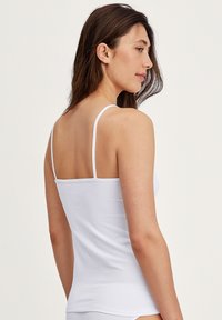 Débardeur blanc à fines bretelles, en coton doux. Design ajusté, dos sans couture, texture lisse, idéal pour le superposition.