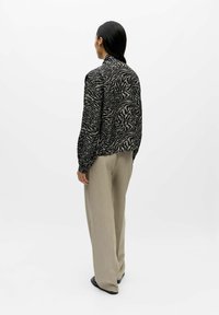 Pitkähihainen paita musta-beige abstrakti kuvio, yhdistetty vaalean beigen sävyisiin leveälahkeisiin housuihin. Sileä kangas ja rento istuvuus.