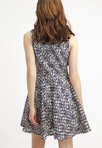 Marineblaues Kleid mit cremefarbener Spitze, ausgestelltem Rock, tailliertem Oberteil und ärmellosem Design, das mit aufwendigen Blumenmustern verziert ist.