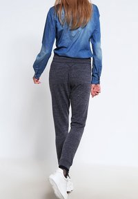 Košile z chambray s vybledlým modrým přechodem, kombinovaná s tmavě šedými tepláky. Bílé tenisky a jemné texturované detaily látky jsou viditelné.