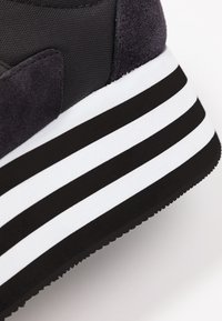 Czarne i szare sneakersy z teksturowanym materiałem. Wyposażone w grubą, prążkowaną czarno-białą podeszwę oraz zamszowy akcent na pięcie.