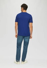 Navy blue cotton t-shirt with short sleeves, paired with light blue denim jeans and white sneakers, viewed from the back.