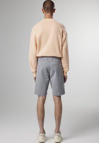 Felpa color pesca chiaro e pantaloni corti grigi, con una vestibilità comoda. I pantaloni corti presentano tasche posteriori. Le calzature sono bianche con accenti color beige.