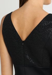 Czarna sukienka z teksturowym wzorem kwiatowym na korpusie. Posiada głęboki dekolt w kształcie V z tyłu oraz dyskretny zamek błyskawiczny. Gładkie satynowe wykończenie poniżej.