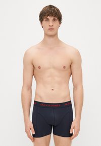 Black boxer briefs made from smooth fabric, featuring a red logo waistband. The design is fitted, with a supportive front pouch.