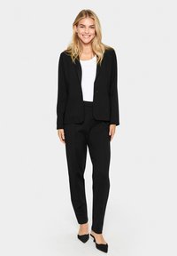 Black tailored suit, single button blazer with notched lapels, slim-fit trousers, paired with a white top and black pointed flats.