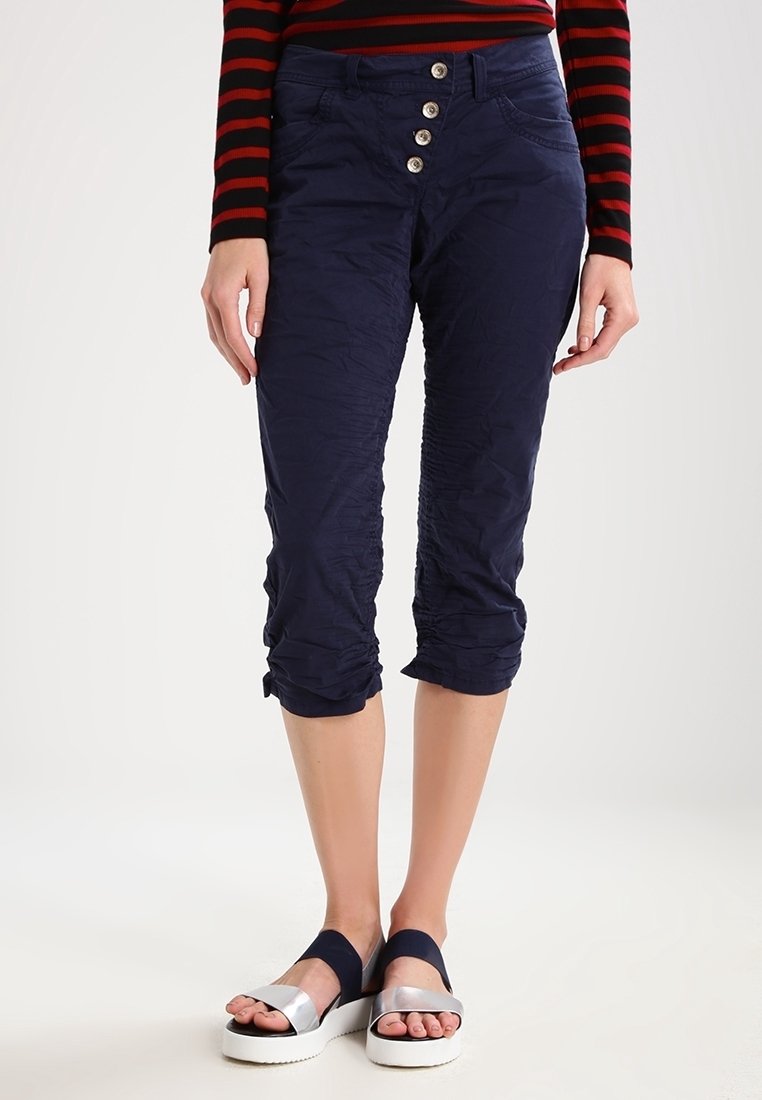 Námořnické modré zkrácené kalhoty s texturovaným povrchem, s pětitlačítkovým zapínáním vpředu a nařasenými manžetami. V kombinaci se stříbrnými a námořnickými sandály.