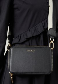 Borsa a tracolla sintetica nera con dettagli in oro, forma rettangolare, dotata di chiusura con zip e una tracolla a contrasto. Logo visibile sul davanti.