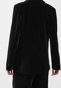 Czarny aksamitny żakiet o strukturalnym designie, z klapami i mankietami zapinanymi na guziki, ukazujący miękką teksturę i czyste linie.