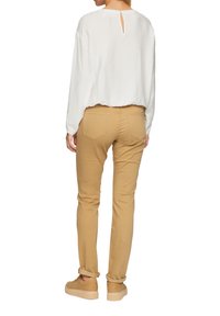 Witte, lichte lange mouwen top met een textuurafwerking en een sleutelgatdetail aan de achterkant, gecombineerd met nauwsluitende tan broek en beige veterschoenen.