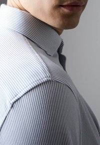 Hellblau-weiß gestreiftes Hemd mit spitzem Kragen und strukturierter Baumwolle, das sichtbare Nähte entlang der Schulter- und Kragennaht aufweist.