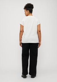 White short-sleeve t-shirt with a round neckline, paired with black wide-leg trousers and black shoes, viewed from the back.