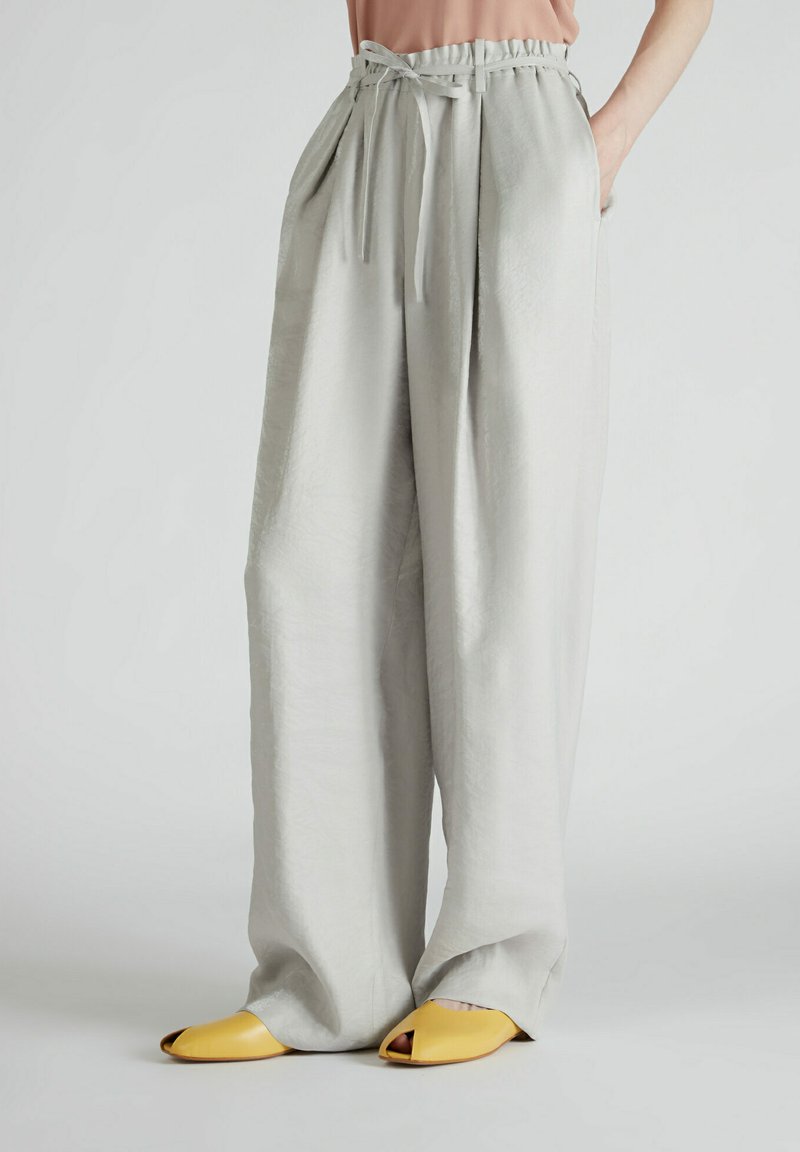 Jasnoszare spodnie szerokie z elastycznym pasem i dwiema bocznymi kieszeniami, wykonane z gładkiego, miękkiego materiału; w połączeniu z żółtymi butami odkrytymi na palcach.