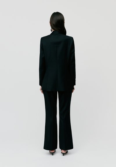 Tailored black suit featuring a fitted blazer and flared trousers. Smooth texture, minimal detailing, with a classic silhouette.