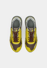 Ζευγάρι κίτρινων και καφέ Reebok αθλητικών παπουτσιών με καφέ κορδόνια, σε θεώρηση από πάνω σε λευκό φόντο.