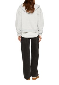 Grauer Hoodie mit lockerer Passform, der dekorative Nieten-Details an den Schultern aufweist, kombiniert mit schwarzen, weit geschnittenen Cargo-Hosen und beigen Schuhen.