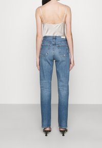 Světle modré džínové kalhoty s vysokým pasem a rovnými nohavicemi, s viditelnými zadními kapsami a jemně vybledlou texturou, v kombinaci se saténovým topem na úzká ramínka.