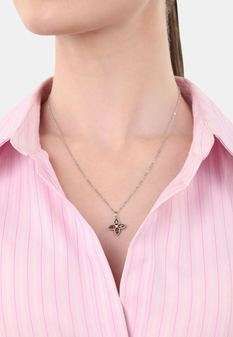Collana d'argento con un pendente floreale che presenta quattro pietre marroni e trasparenti, indossata sopra una camicia a righe rosa chiaro, esponendo l'area del collo.