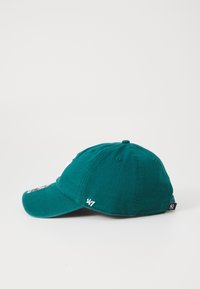 Green cotton baseball cap with a curved brim, embroidered logo on the front, and a side label. Designed with eyelets for ventilation.