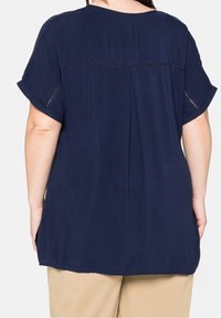 Námořnická modrá halenka s krátkým rukávem a volným střihem, která má ozdobnou prošívanou linku na horní části zad a boční rozparky na lemu.