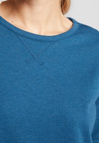 Sweatshirt bleu avec un col rond, tissu texturé et détails de couture visibles au niveau du col et de l'épaule. Surface lisse.