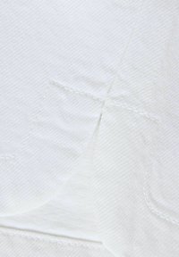 Κοντινό πλάνο λευκού υφάσματος με λεπτομερείς ραφές και επικαλυπτόμενα ραφικά, που αναδεικνύουν την υφή και την τέχνη της ραπτικής.